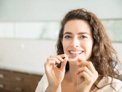 Portrait of beautiful patient holding orthodontic retainers in dental clinic